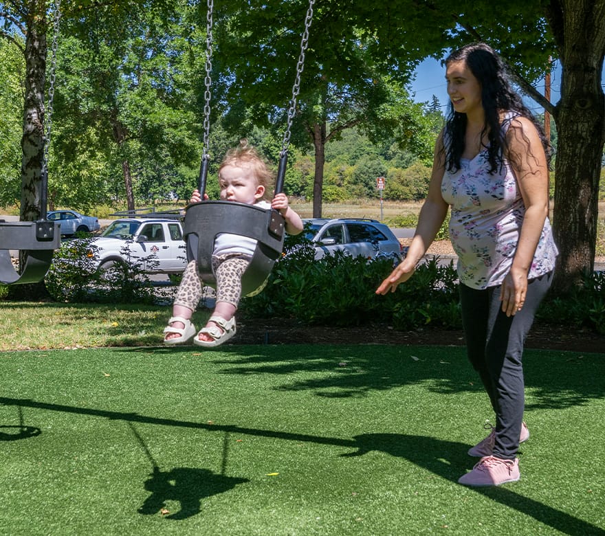 Mother pushes her baby on a swing at the park