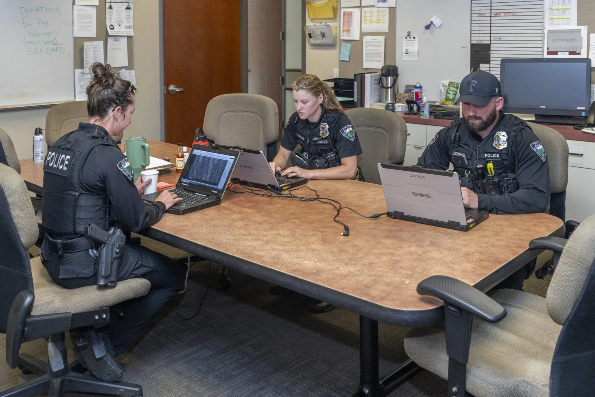 Police officers in uniform sitting at a conference table on their laptops