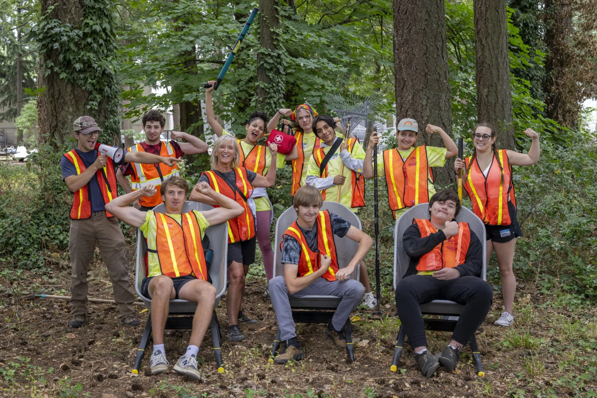 Group of youth wearing safety vests in the woods, smiling at the camera