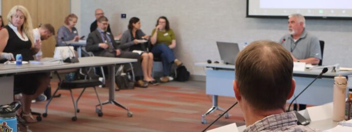 Adults in business clothing sit in a conference room during a large meeting