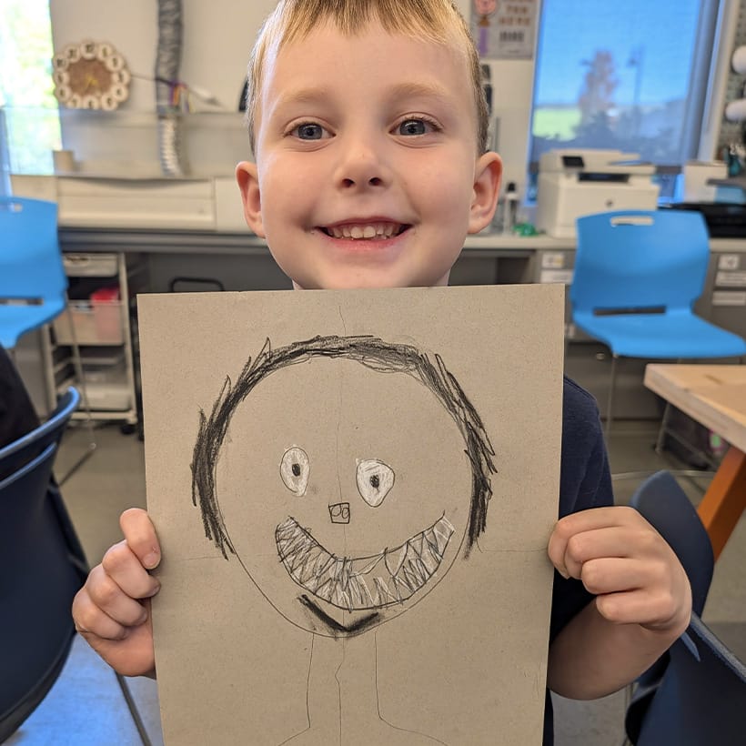 Young boy smiles and holds up a drawing he made